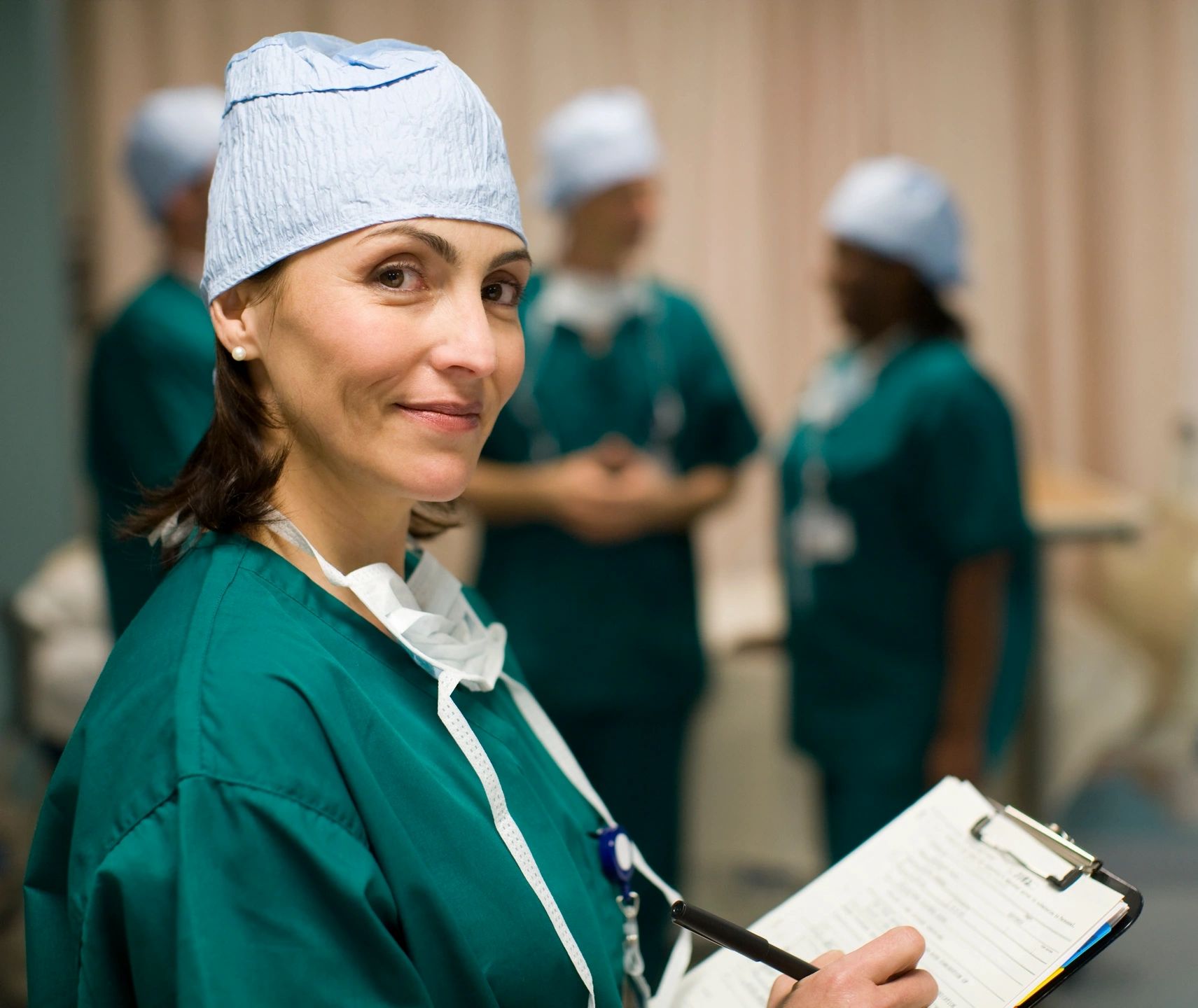 Female physician in scrubs holding a clipboard and smiling toward camera