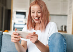 Image of delighted woman playing video game on mobile phone while sitting on sofa at home