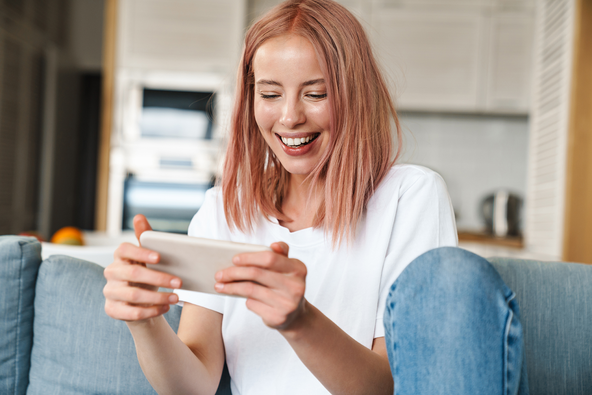 Image of delighted woman playing video game on mobile phone while sitting on sofa at home