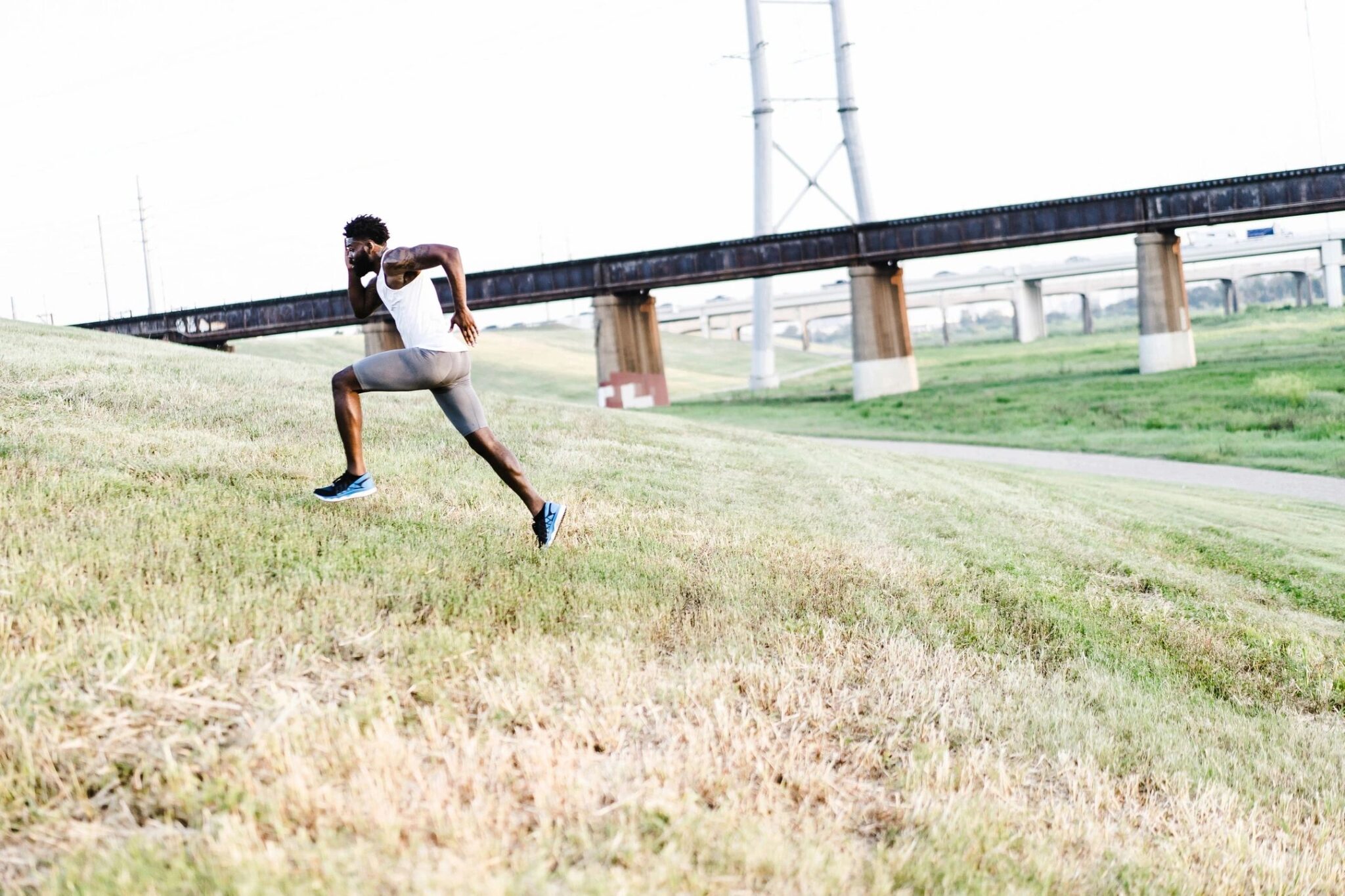 Man running up a steep hill with a bridge in the background.