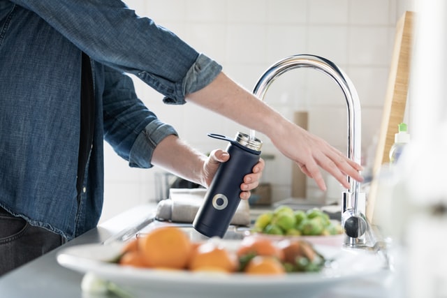 A person fills a water bottle from a sink faucet.