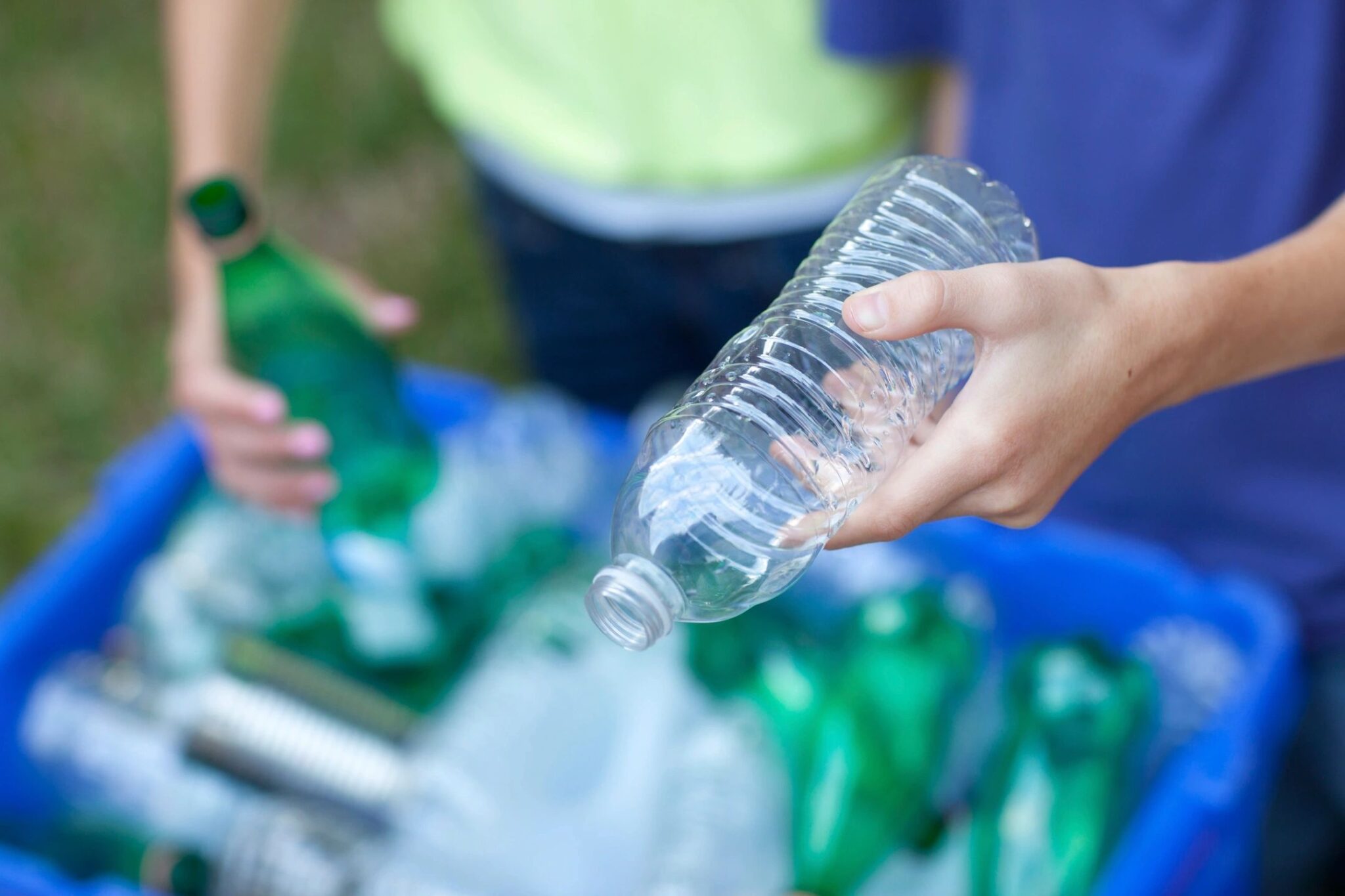 People putting plastic bottles in recycling bin.