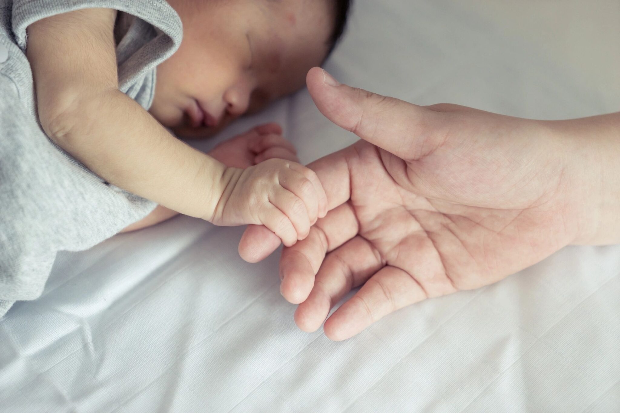 An adult hand reaches out and a newborn baby grasps the adult's index finger