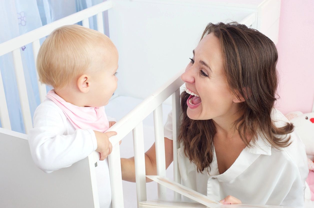 babies' brains recognize faces at a younger age than thought, such as this infant in a crib facing a smiling adult woman