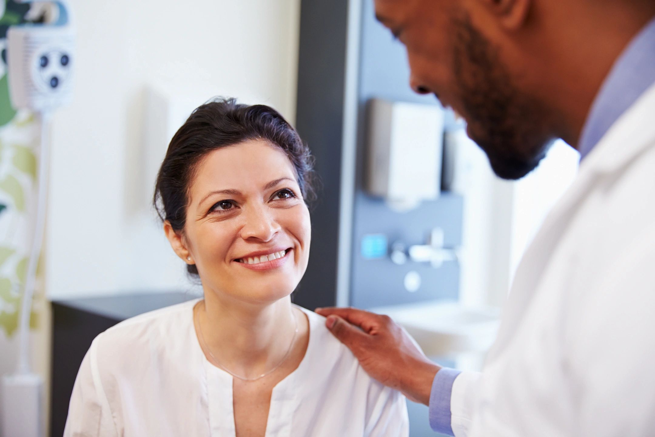 woman, seated, smiling up at doctor who has his hand on her shoulder, suggesting positive medical step such as getting an influenza vaccine